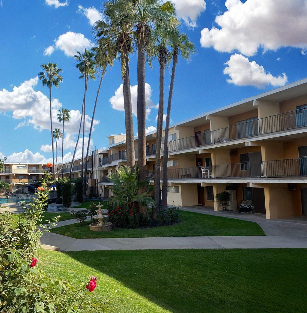 A sunny day at the apartment complex with palm trees and red flowers in the foreground.