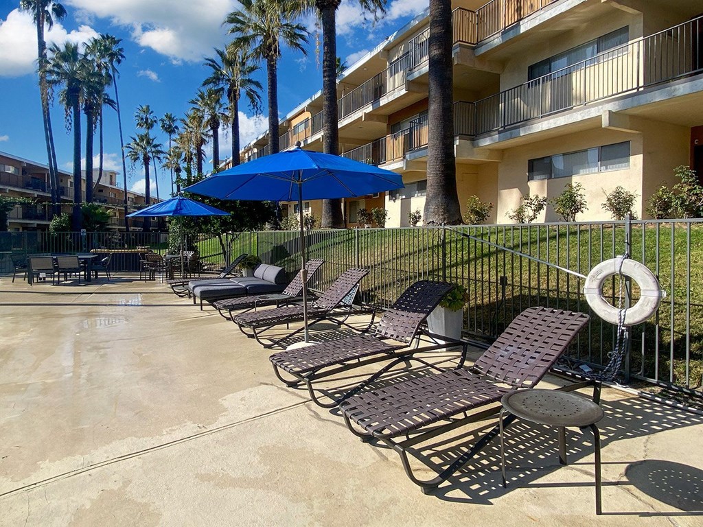 A pool area with chairs and umbrellas in front of a building.