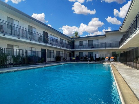 A swimming pool is surrounded by a black fence and a building with balconies.
