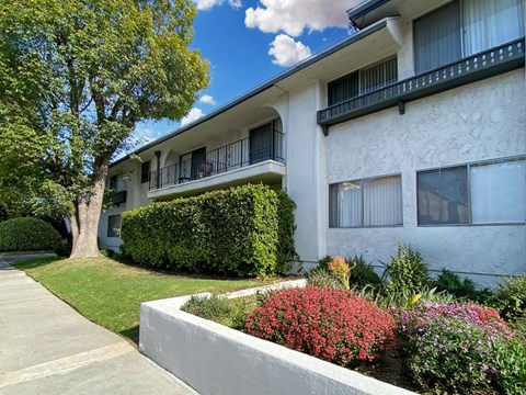 A white building with a balcony and a green tree.
