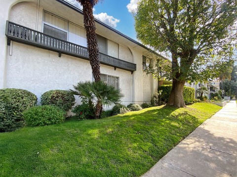 A white building with a balcony and a tree in front of it.