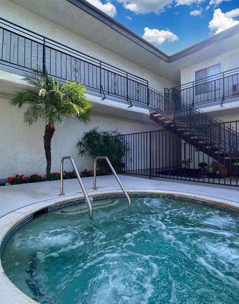A hot tub sits in the middle of a patio with a palm tree and a staircase in the background.