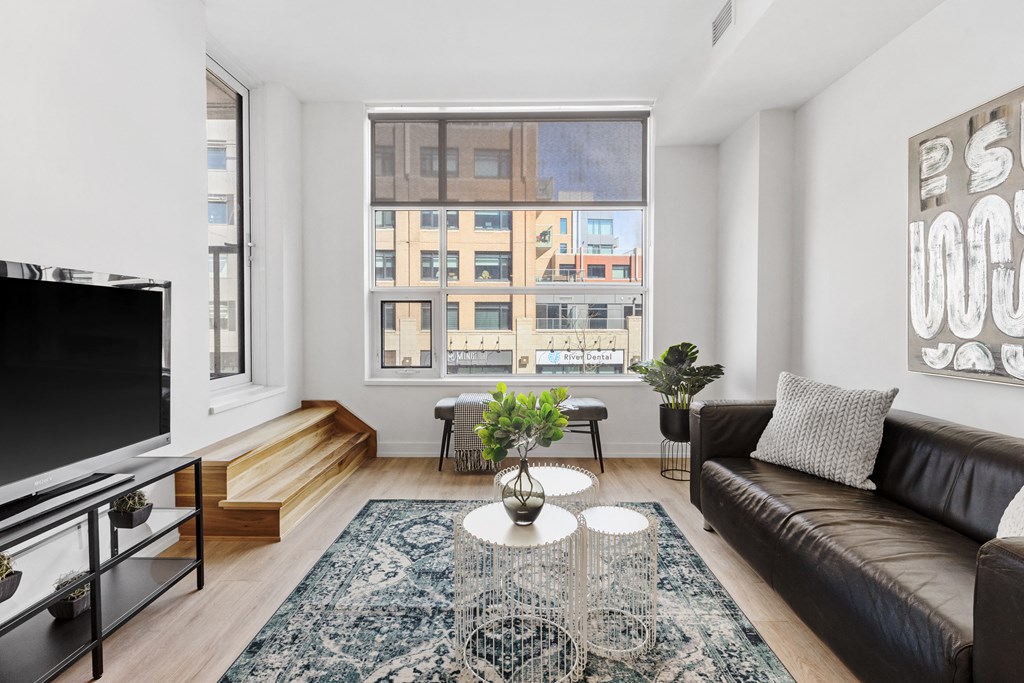 A living room with a black couch, a television, and a large window.