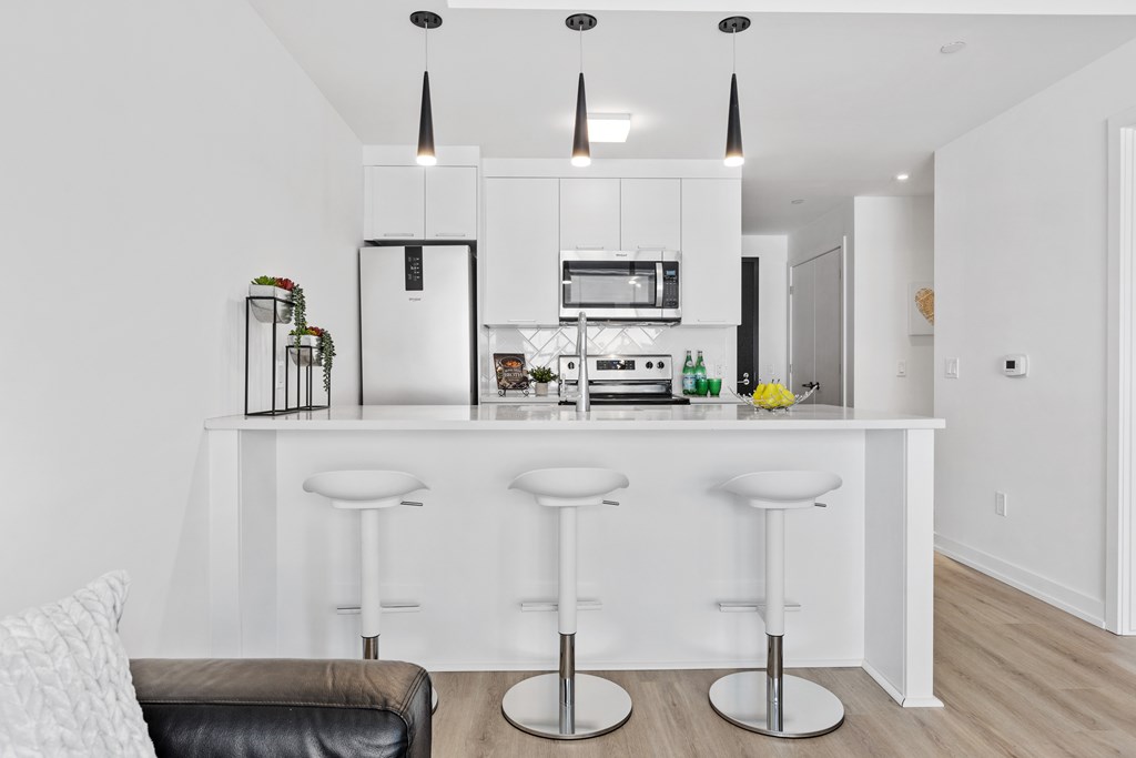 A modern kitchen with white cabinets and a bar area with stools.