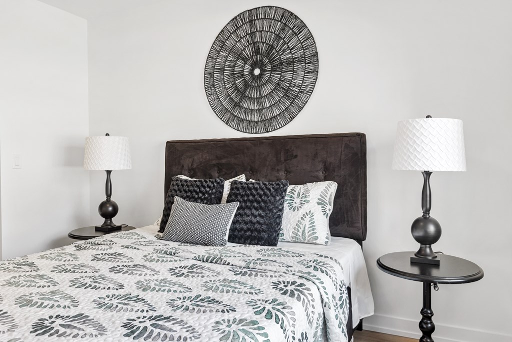 A bed with a white and grey comforter and a dark headboard with a round decoration on the wall.