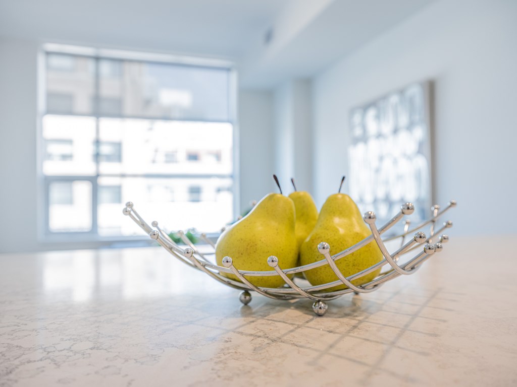 Two yellow pears in a metal fruit basket on a marble table.