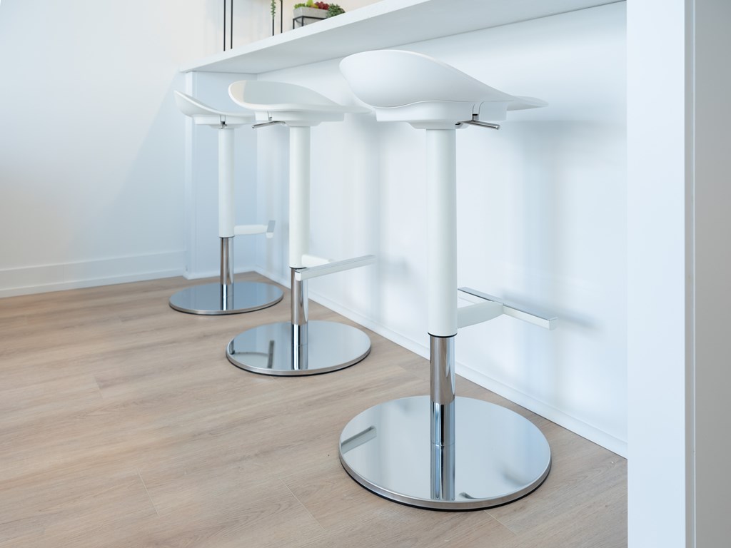 Three white bar stools with chrome legs and tops are placed in a row.
