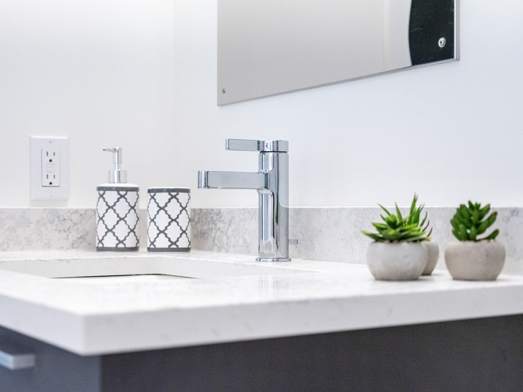 A bathroom sink with a mirror above it and two small potted plants on the counter.