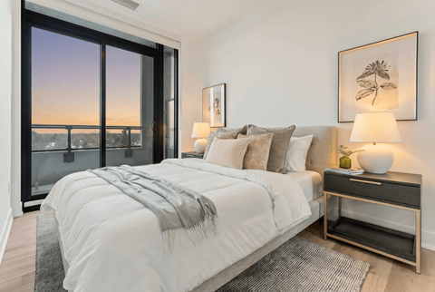 A bedroom with a large bed and a view of the city at dusk.