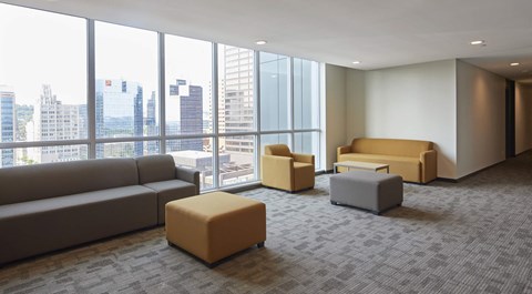 A room with a large window overlooking a cityscape and furniture including a sofa, ottoman, and chair.