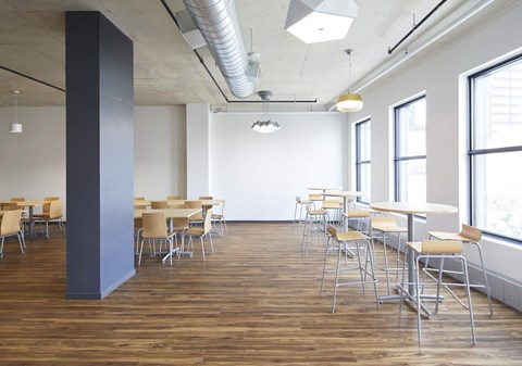 A room with wooden floors and white walls has tables and chairs.