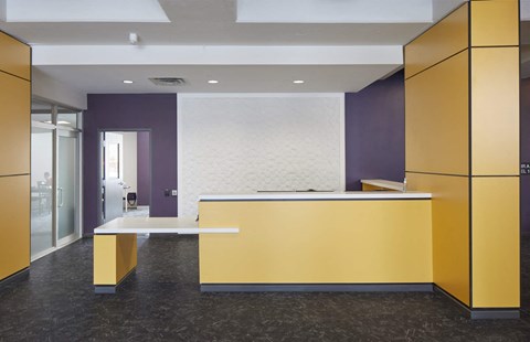 A reception area with a yellow counter and a white bench.