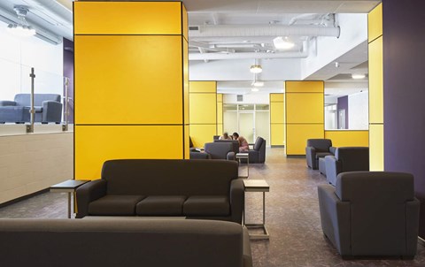 A yellow partition divides a room with black couches.