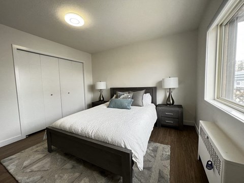 A bedroom with a bed, nightstand, and a window.