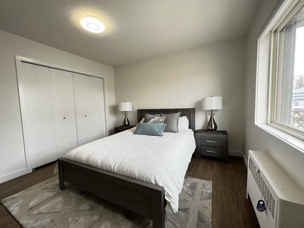 A bedroom with a bed, nightstand, and a window.