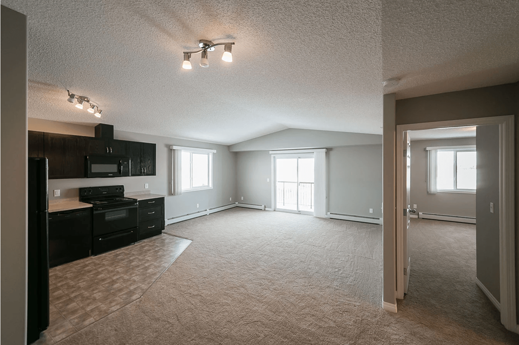 A spacious living room with a kitchen area to the left and a doorway leading to another room to the right.