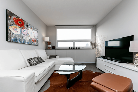 A living room with a white couch, a brown ottoman, and a painting on the wall.