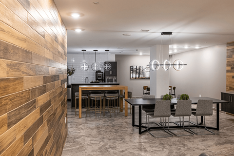 A modern dining room with a wooden wall on the left and a black table with grey chairs.
