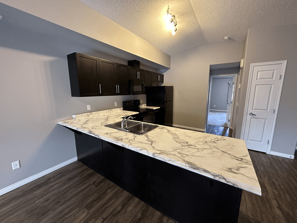 A kitchen with a marble countertop and black cabinets.