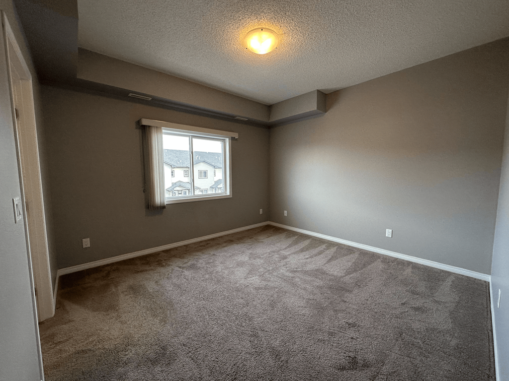 A room with a carpeted floor and a window with a view of buildings outside.