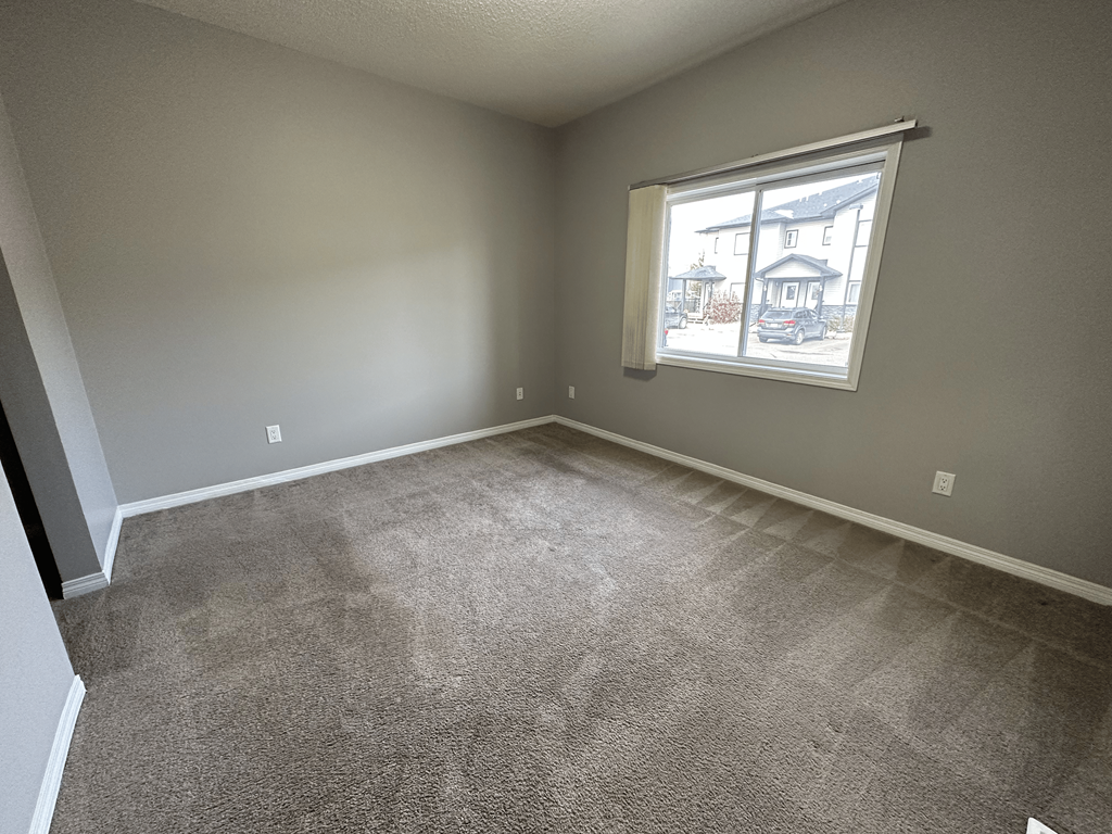 A room with a carpeted floor and a window showing a house outside.