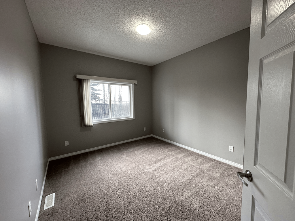 A room with a carpeted floor and a window with a white curtain.