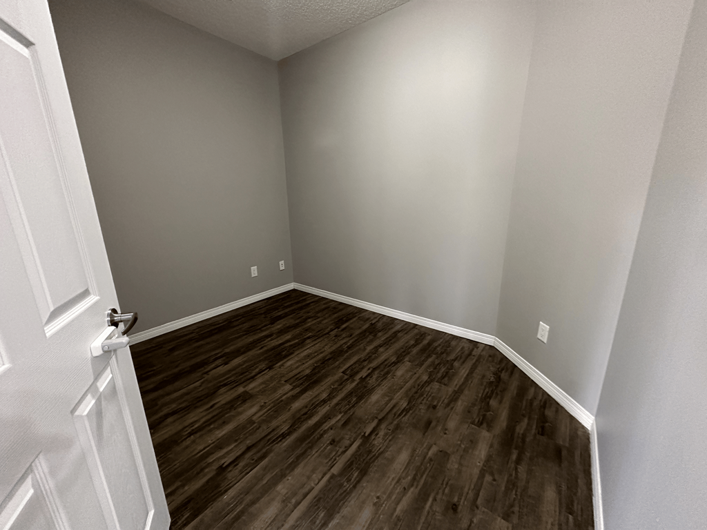 A room with a white door and wood flooring.