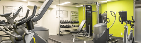 A gym with a yellow wall and a variety of exercise equipment.