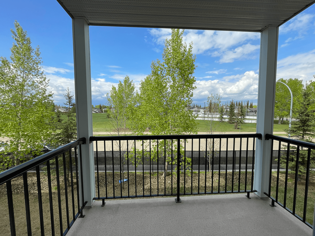 A balcony with a black railing and a view of a green lawn and trees.