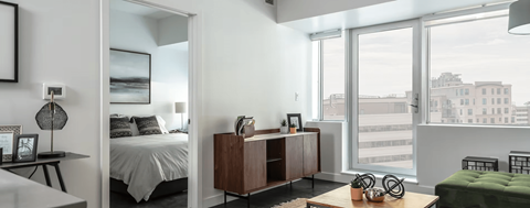 A bedroom with a bed, a nightstand, a chair, and a window overlooking a cityscape.