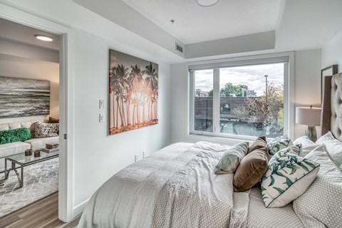 A bedroom with a large bed and a painting of palm trees on the wall.