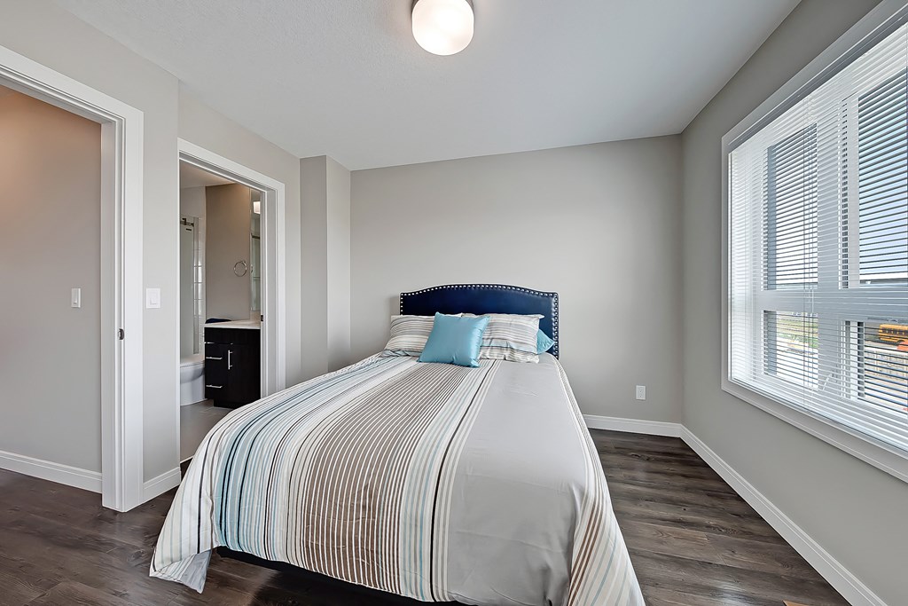 A bedroom with a bed, striped comforter, and a window with blinds.