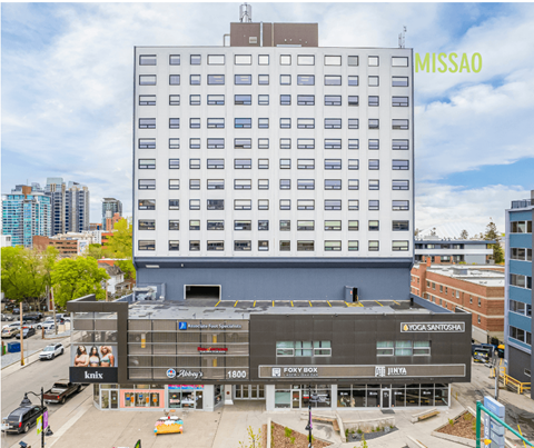 A street view of a city with a large building in the background and a smaller building in the foreground with various businesses.