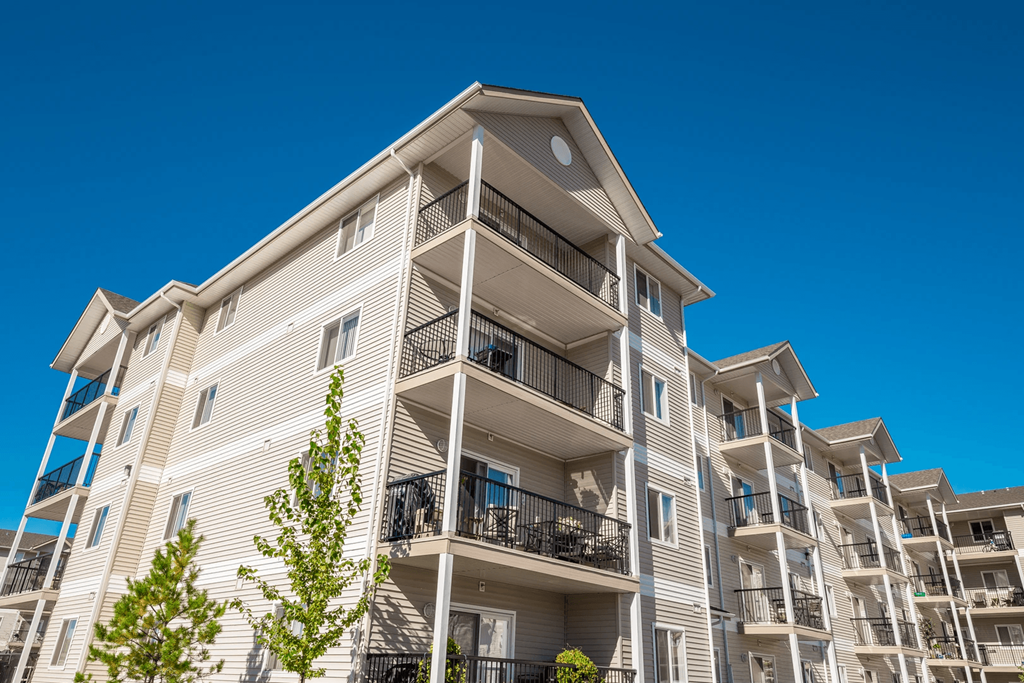 A tall apartment building with balconies and trees in front.