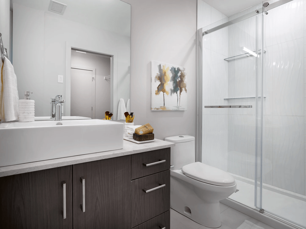 A bathroom with a white sink, toilet, and a glass shower stall.
