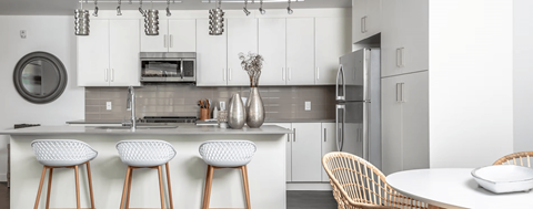 A modern kitchen with white cabinets and a white island with three stools.