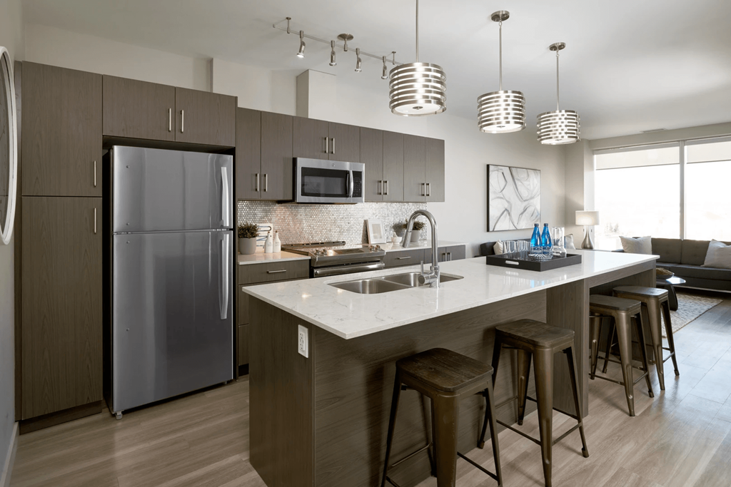 A modern kitchen with a refrigerator, microwave, and bar stools.