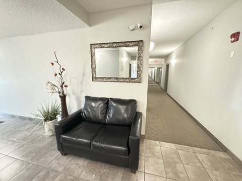 A black leather couch sits in a hallway with a mirror above it.