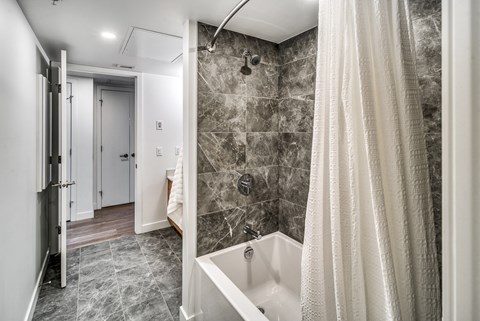 A bathroom with a marble tile wall and a white bathtub.