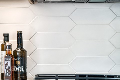 Two bottles of olive oil are in front of a white tiled wall.