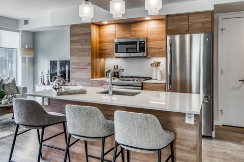 A modern kitchen with a stainless steel refrigerator, a microwave above the stove, and a breakfast bar with chairs.
