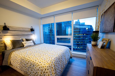 A bedroom with a bed, nightstand, and window overlooking a cityscape.