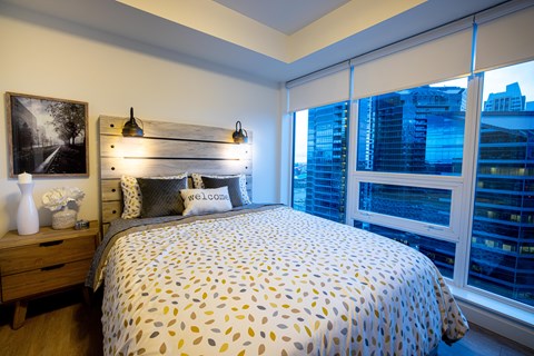 A bedroom with a bed, a nightstand, and a window with blinds.