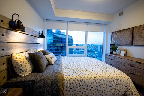 A bedroom with a bed, pillows, and a window overlooking a cityscape.