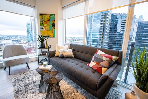 A living room with a brown couch and a large window overlooking a city.