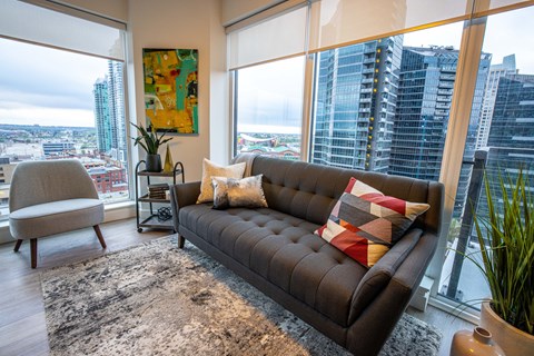 A living room with a brown couch and a large window overlooking a cityscape.