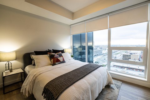 A bedroom with a large bed and a city view through the window.