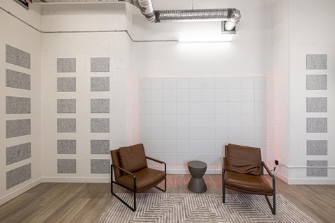 A room with a chair, ottoman, and a table with a metal pipe on the ceiling.