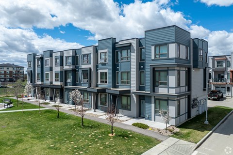 A row of modern townhouses with a sidewalk and trees in front.