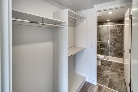 A white walk-in closet with a sliding door open to a bathroom.